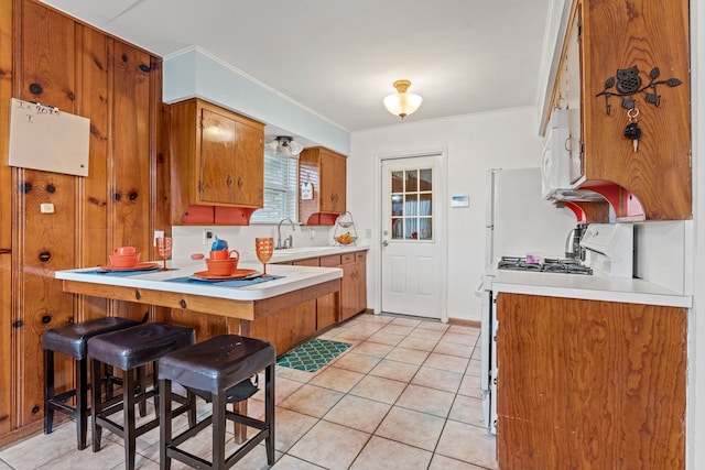 kitchen featuring light tile patterned floors, sink, a breakfast bar area, white range with gas cooktop, and kitchen peninsula