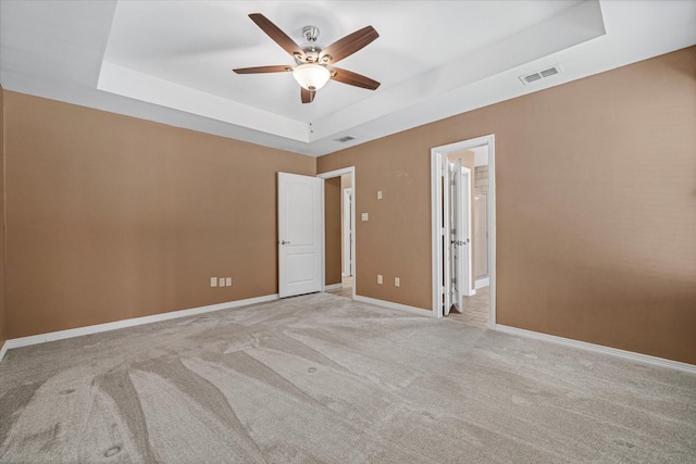 empty room with light colored carpet, a raised ceiling, and ceiling fan