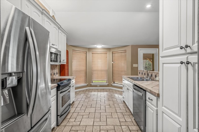 kitchen with white cabinetry, appliances with stainless steel finishes, tile counters, and sink