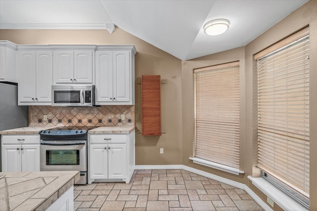 kitchen with lofted ceiling, white cabinetry, tile countertops, appliances with stainless steel finishes, and backsplash