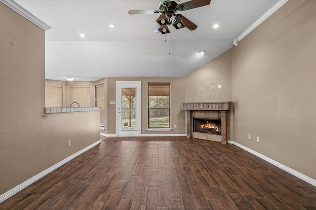 unfurnished living room with dark wood-type flooring, crown molding, vaulted ceiling, ceiling fan, and a tiled fireplace