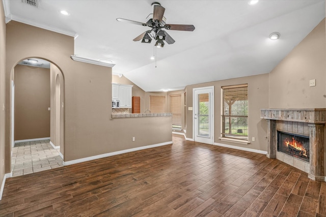 unfurnished living room featuring lofted ceiling, dark wood-type flooring, ceiling fan, a fireplace, and ornamental molding