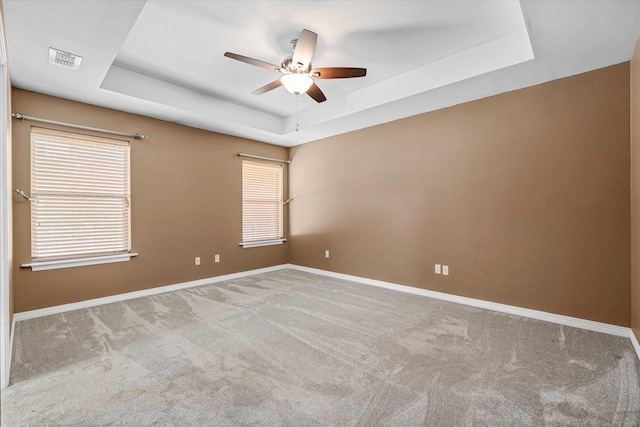 carpeted spare room with a raised ceiling and ceiling fan