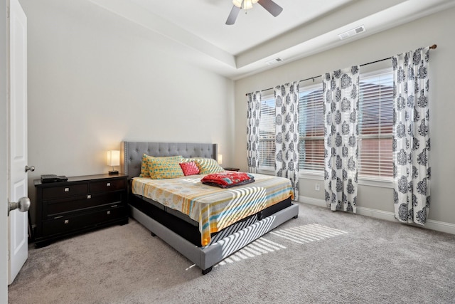 bedroom featuring ceiling fan, light colored carpet, and a tray ceiling