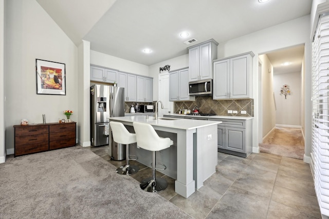 kitchen featuring sink, appliances with stainless steel finishes, gray cabinetry, an island with sink, and a kitchen bar