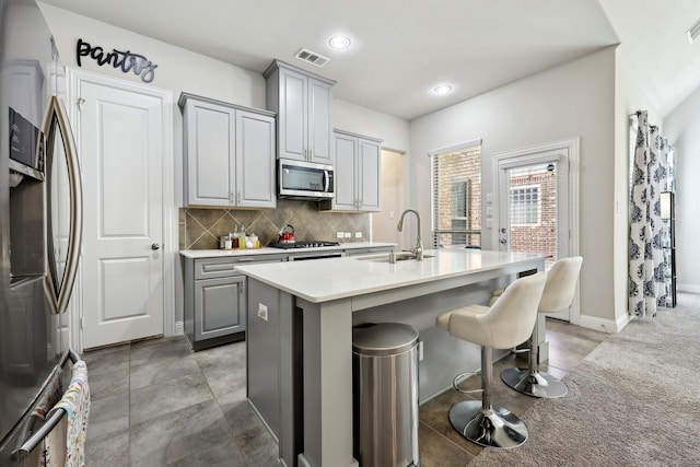 kitchen featuring sink, a breakfast bar area, appliances with stainless steel finishes, gray cabinets, and an island with sink