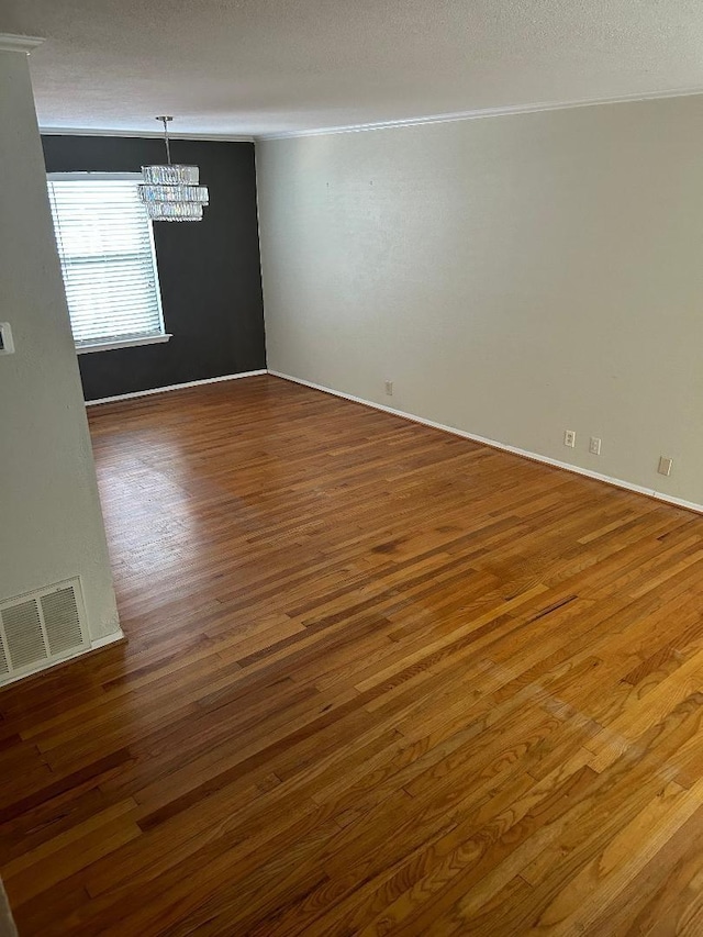 empty room with ornamental molding, hardwood / wood-style floors, a textured ceiling, and a notable chandelier