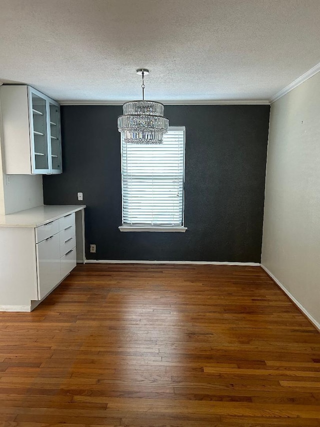 unfurnished dining area with ornamental molding, dark hardwood / wood-style floors, a chandelier, and a textured ceiling