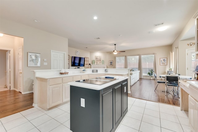 kitchen with black electric stovetop, light tile patterned floors, ceiling fan, and a kitchen island