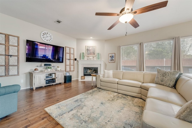 living room featuring ceiling fan, wood-type flooring, and a tile fireplace