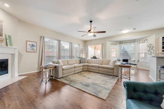 living room with a tile fireplace, plenty of natural light, wood-type flooring, and ceiling fan