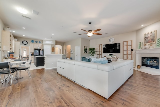 living room with a tile fireplace, ceiling fan, and light hardwood / wood-style flooring