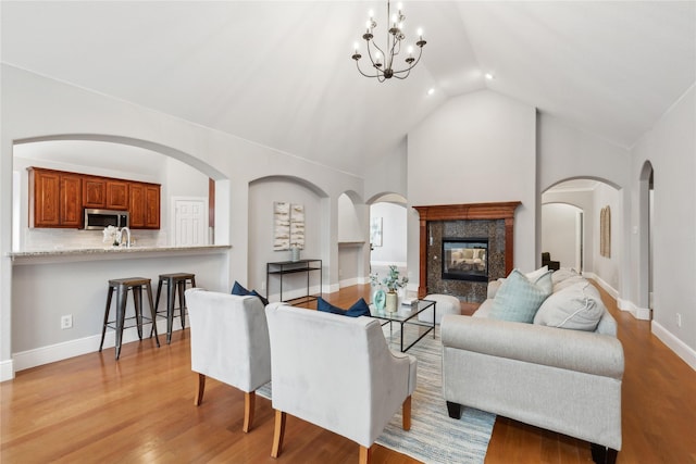 living room featuring sink, light hardwood / wood-style flooring, an inviting chandelier, high vaulted ceiling, and a fireplace