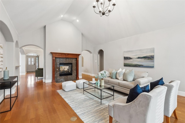 living room featuring high vaulted ceiling, hardwood / wood-style floors, a tile fireplace, and a notable chandelier