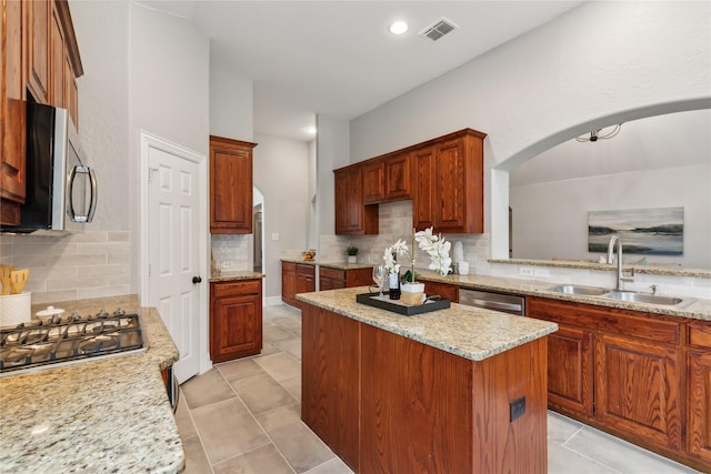 kitchen with sink, stainless steel appliances, a center island, light stone counters, and decorative backsplash