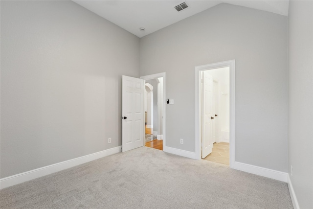 unfurnished bedroom with ensuite bathroom, high vaulted ceiling, and light carpet