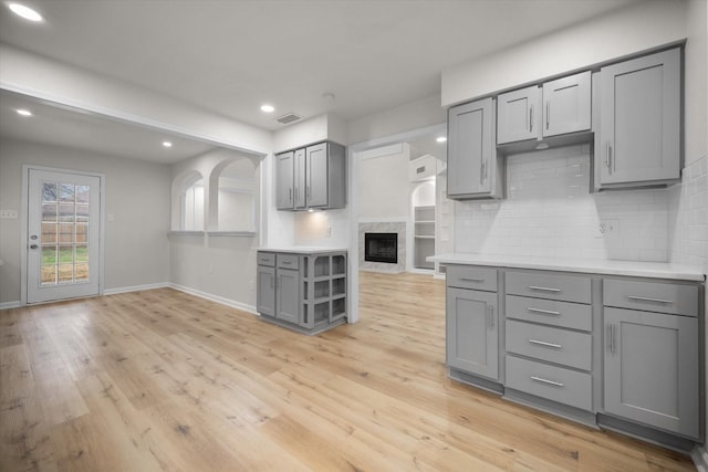 kitchen with gray cabinetry, a fireplace, tasteful backsplash, and light hardwood / wood-style floors