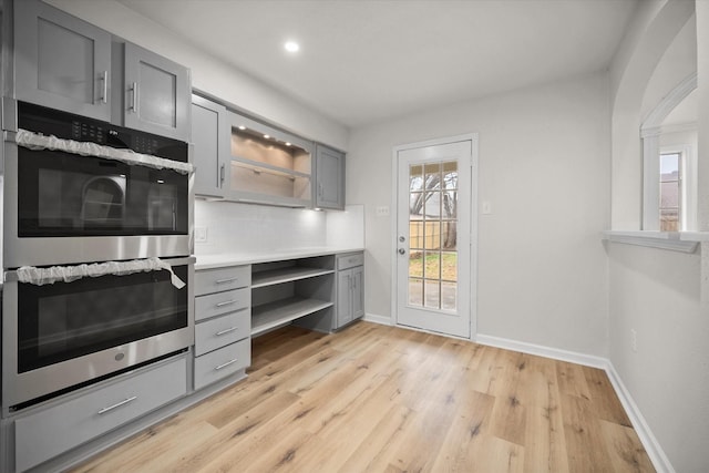 kitchen with gray cabinetry, double oven, backsplash, and a wealth of natural light