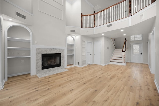 unfurnished living room with a high ceiling, built in features, light hardwood / wood-style floors, and a fireplace