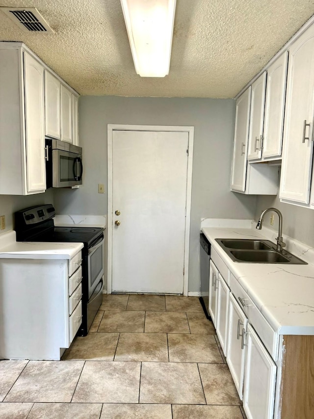 kitchen with sink, white cabinets, light tile patterned floors, stainless steel appliances, and a textured ceiling