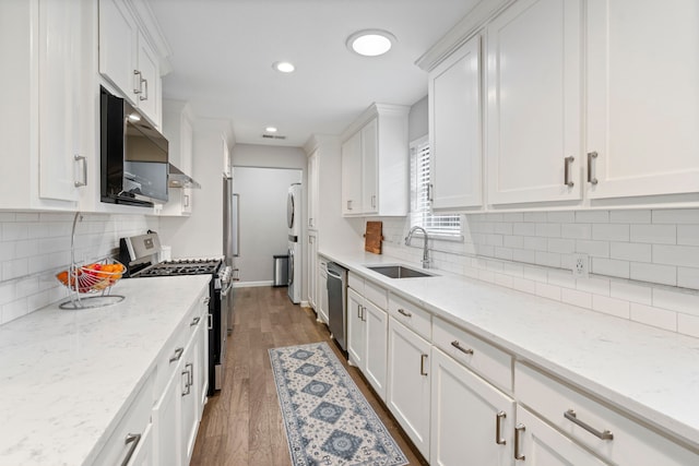 kitchen with sink, appliances with stainless steel finishes, dark hardwood / wood-style flooring, light stone countertops, and white cabinets