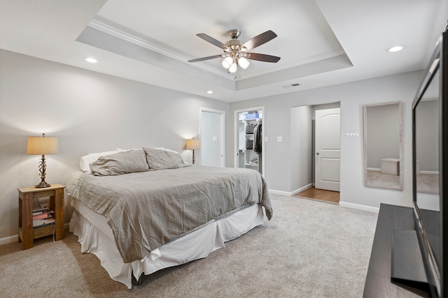 bedroom featuring a spacious closet, light carpet, ornamental molding, a raised ceiling, and a closet