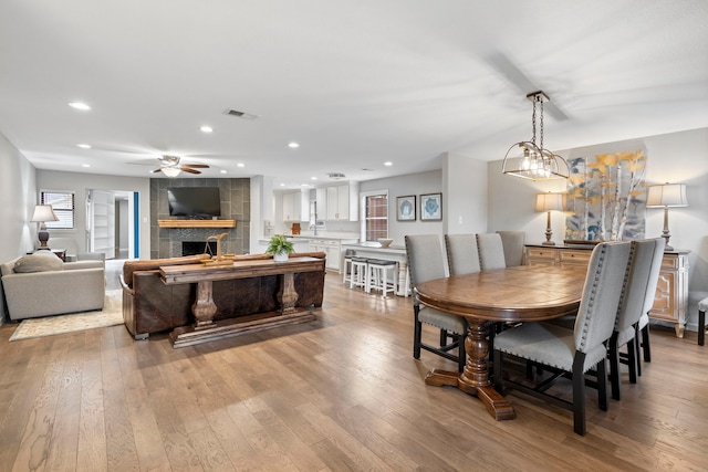 dining space featuring light hardwood / wood-style floors, a large fireplace, and ceiling fan