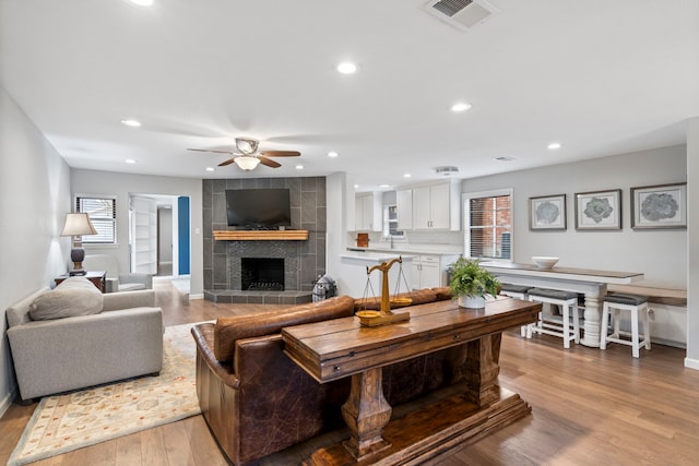 living room with ceiling fan, a tiled fireplace, and light hardwood / wood-style floors