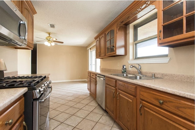 kitchen featuring sink, a textured ceiling, light tile patterned floors, appliances with stainless steel finishes, and ceiling fan