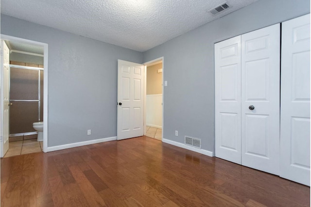 unfurnished bedroom featuring ensuite bathroom, dark hardwood / wood-style floors, a closet, and a textured ceiling