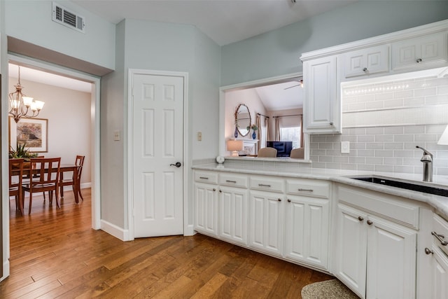 kitchen featuring sink, ceiling fan with notable chandelier, white cabinetry, light hardwood / wood-style floors, and decorative backsplash