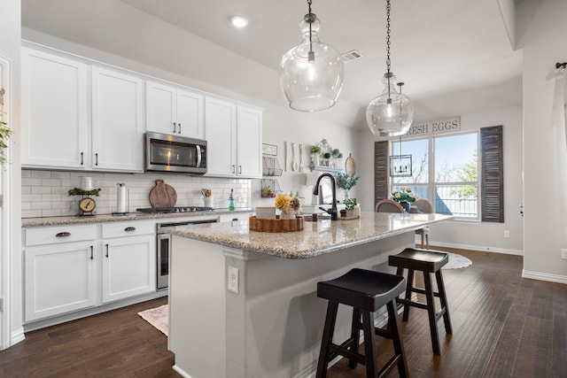 kitchen featuring white cabinetry, appliances with stainless steel finishes, a kitchen island with sink, and hanging light fixtures