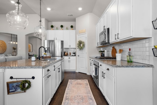 kitchen featuring white cabinetry, stainless steel appliances, a center island with sink, and stone counters