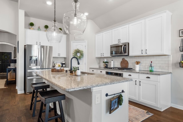 kitchen with sink, appliances with stainless steel finishes, light stone countertops, an island with sink, and white cabinets