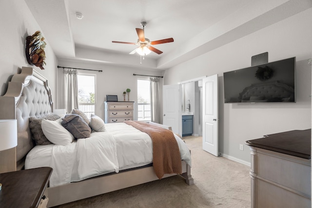 carpeted bedroom featuring ceiling fan, ensuite bathroom, and a raised ceiling