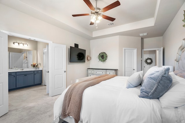 carpeted bedroom with ensuite bathroom, sink, ceiling fan, and a tray ceiling