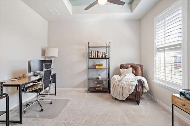 office space featuring a raised ceiling, light colored carpet, and ceiling fan