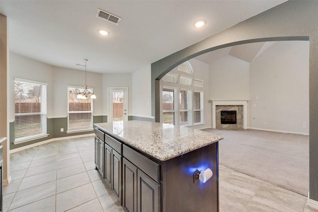 kitchen with hanging light fixtures, dark brown cabinets, a high end fireplace, light stone countertops, and a kitchen island