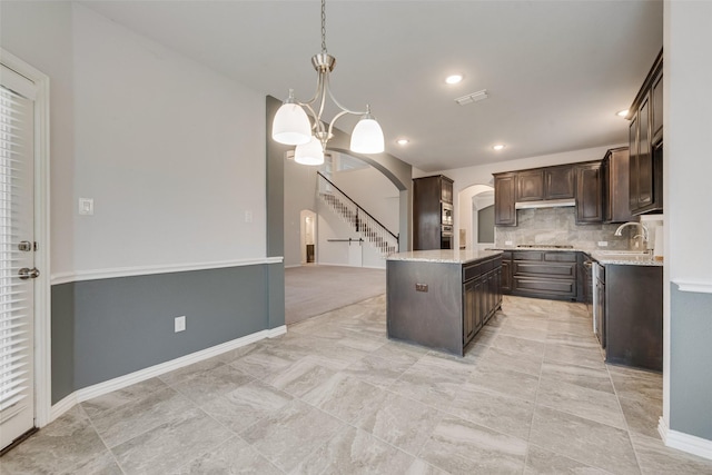 kitchen featuring decorative light fixtures, dark brown cabinets, a kitchen island, a notable chandelier, and decorative backsplash