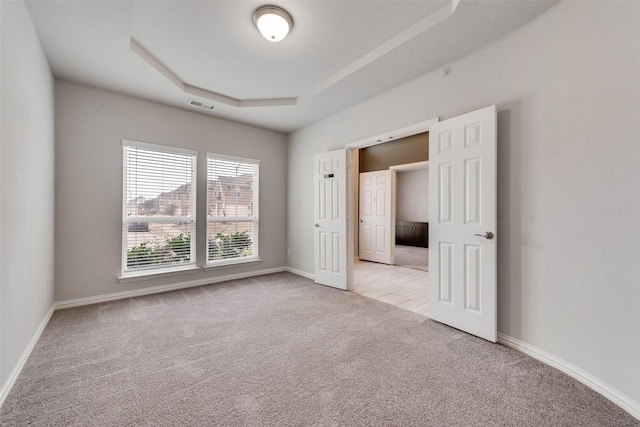 unfurnished bedroom with a raised ceiling and light colored carpet