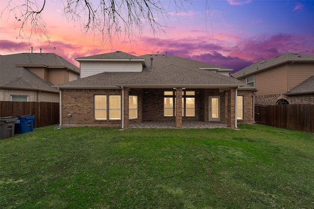 back house at dusk featuring a lawn and a patio