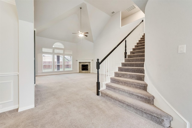 staircase with a fireplace, high vaulted ceiling, ceiling fan, and carpet