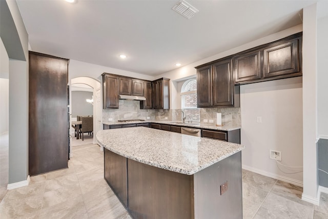 kitchen featuring sink, light stone counters, dark brown cabinets, a kitchen island, and backsplash