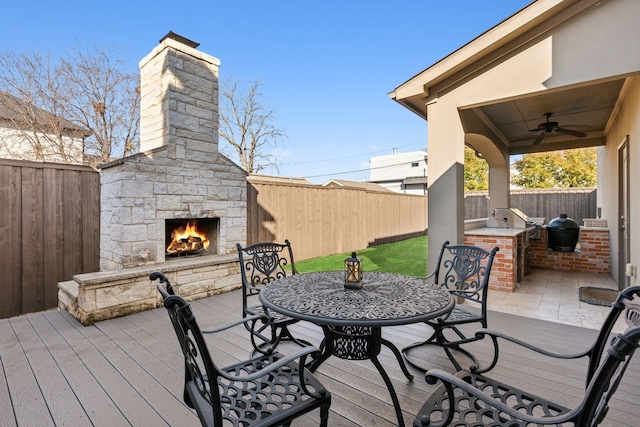 deck featuring ceiling fan, grilling area, exterior kitchen, and an outdoor stone fireplace