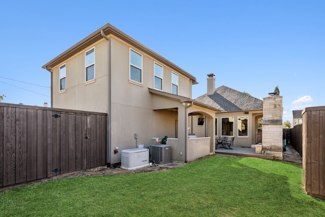 rear view of house with central AC unit, a yard, a stone fireplace, and a patio