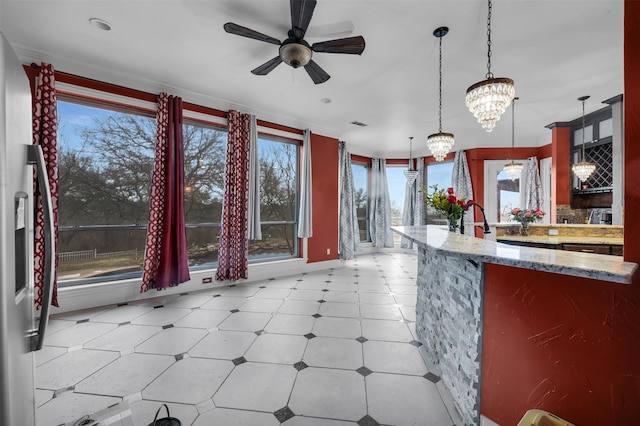 kitchen featuring light stone counters, hanging light fixtures, and ceiling fan with notable chandelier