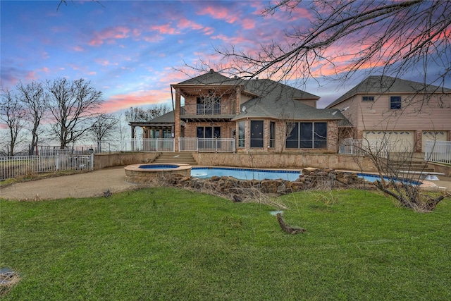 back house at dusk with an in ground hot tub, a balcony, and a yard