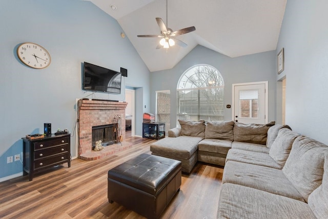 living room with hardwood / wood-style flooring, ceiling fan, a brick fireplace, and high vaulted ceiling