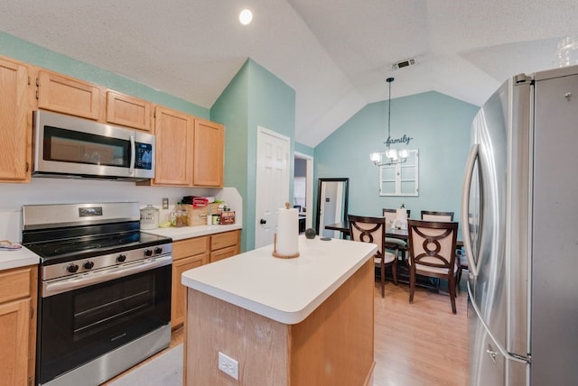 kitchen with pendant lighting, appliances with stainless steel finishes, a center island, light brown cabinetry, and vaulted ceiling