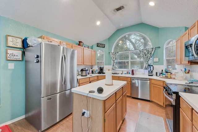 kitchen featuring vaulted ceiling, light wood-type flooring, a center island, stainless steel appliances, and a textured ceiling